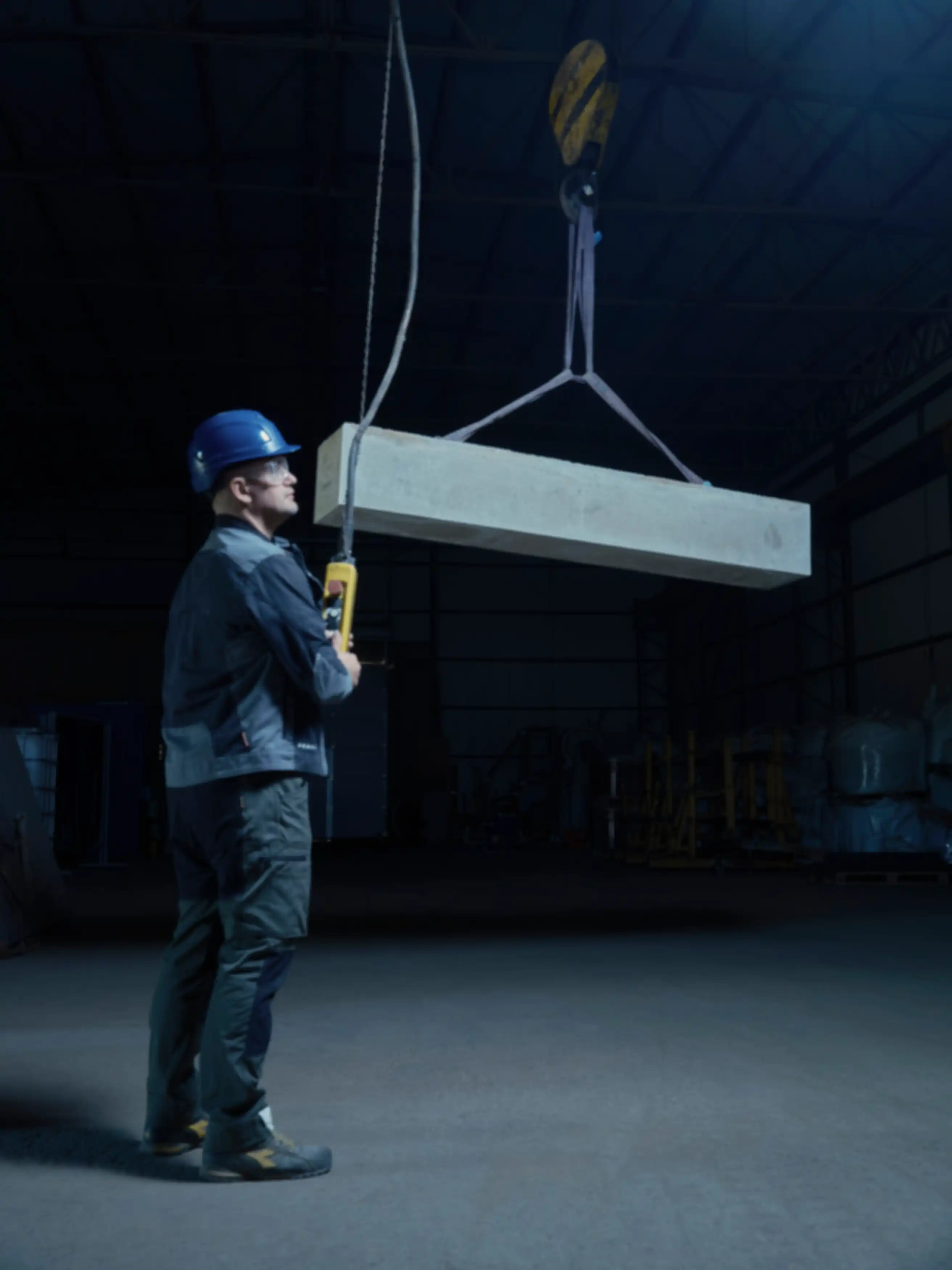A cement block held by a crane. A man is standing in front of it.