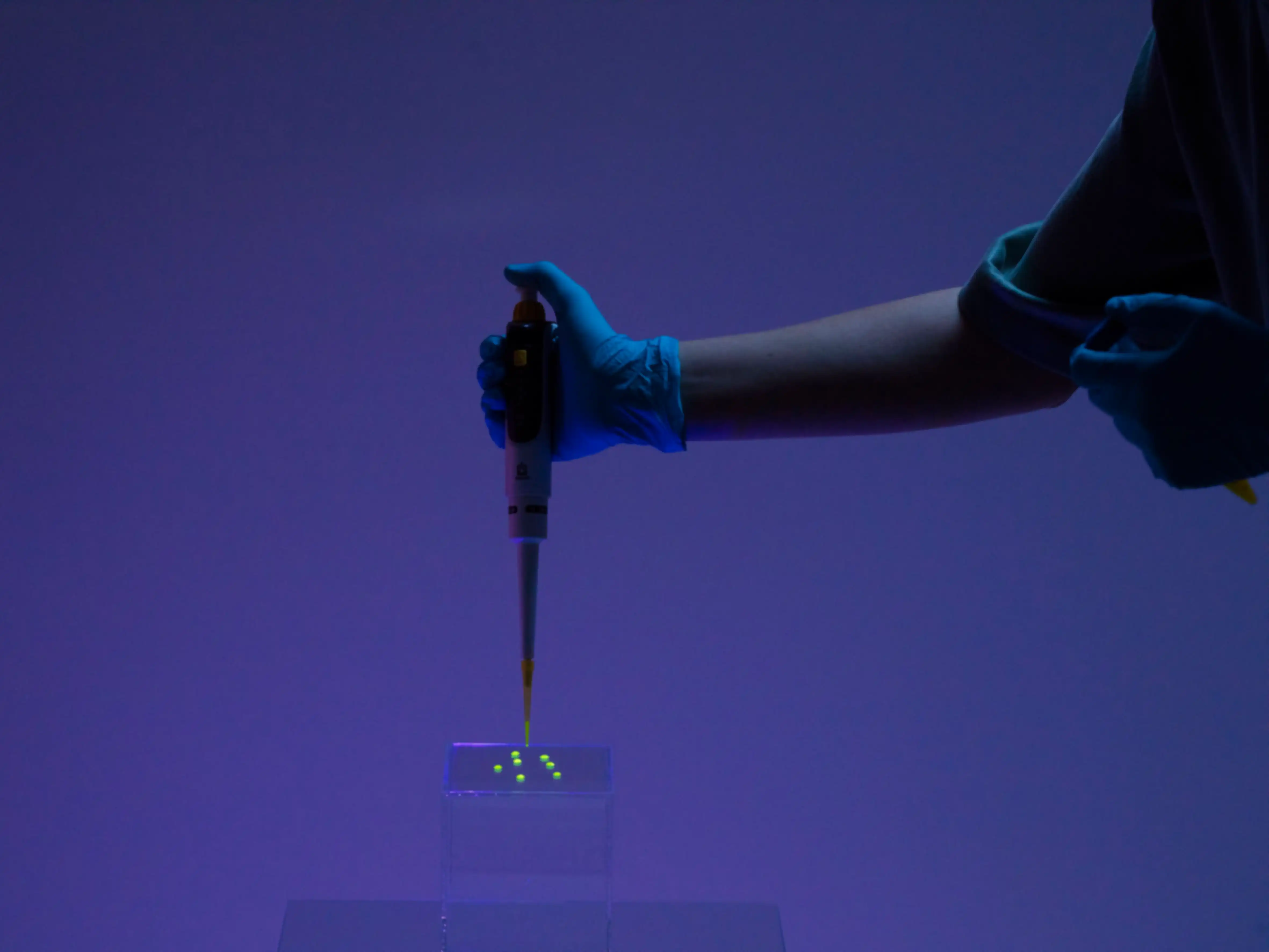 A person is dripping a yellow liquid onto a glass cube using a pipette