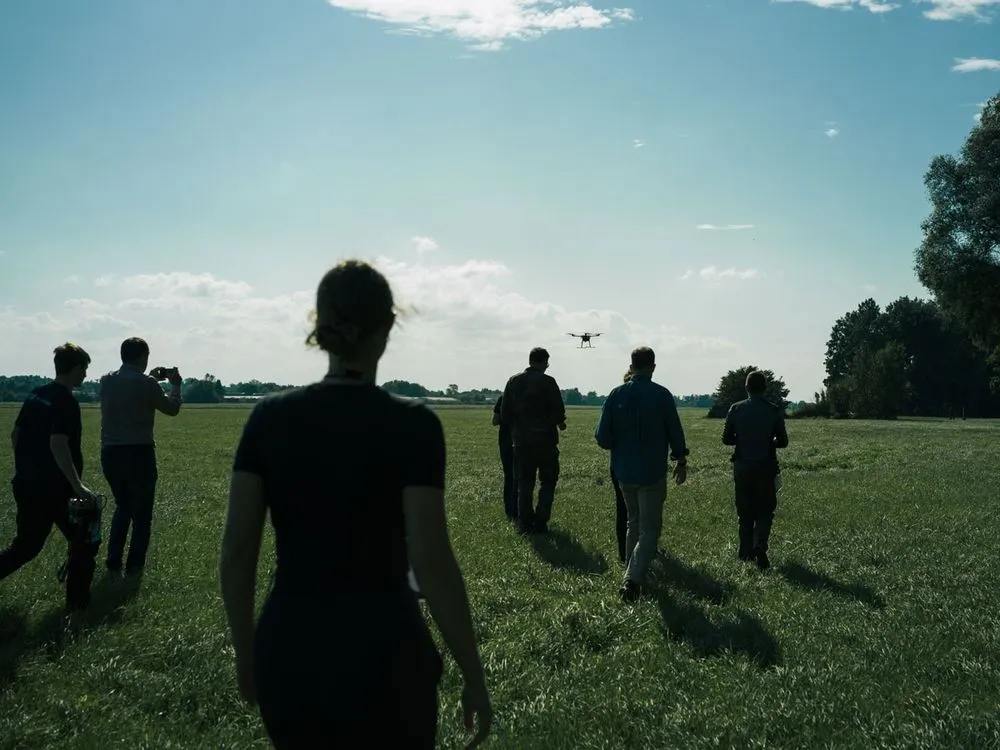 Menschen folgen einer Drohne zu Fuß auf einem weiten Feld